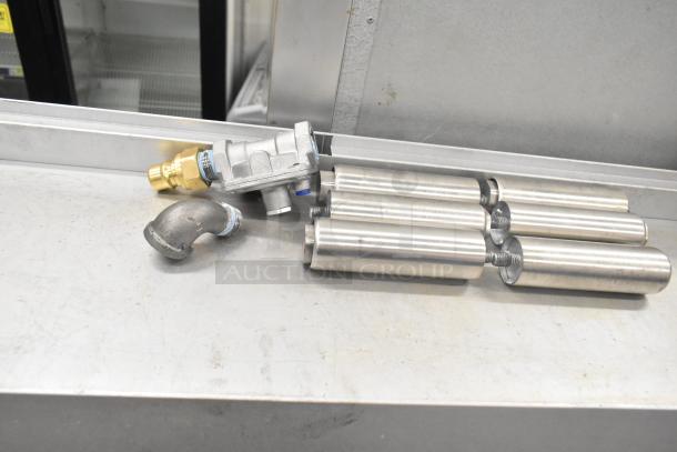 Components for Mainstreet 541E60N gas range, featuring valve and burner tubes, displayed on a stainless steel surface.