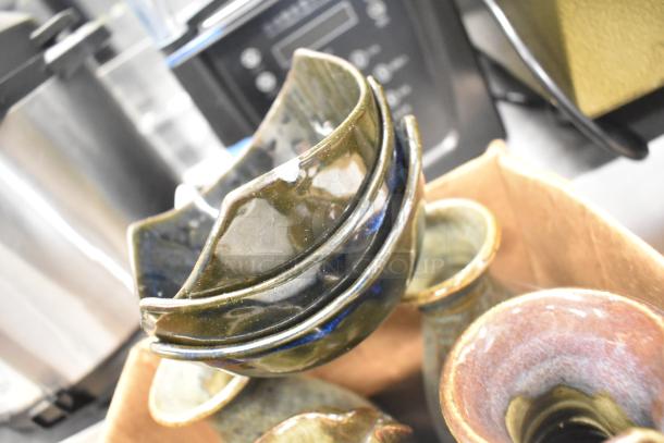 Ceramic bowls, vases, and poly trays in assorted colors and finishes, some with visible wear, arranged in a box.