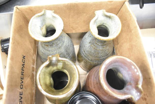 Lot of ceramic vases with textured glaze, earthy tones in cardboard box, showing signs of use. Marking: "REMOVE OVERPACK."