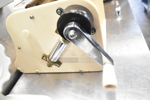 Manual pasta roller featuring a white handle on a metal crank, in good condition on a stainless steel surface.