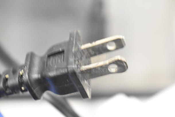 Close-up of a black electrical plug for an appliance, highlighting metal prongs and plastic body.