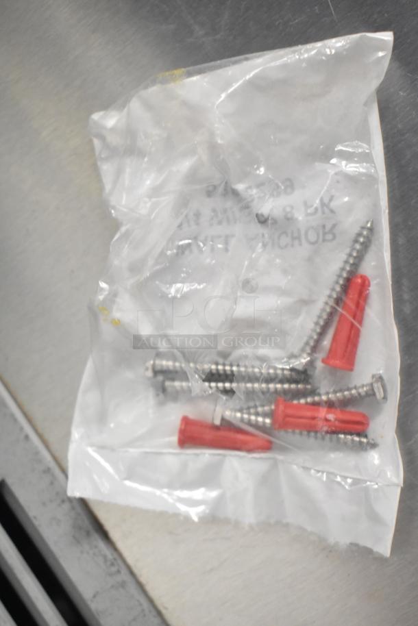 Bag of screws and red wall anchors lying on a metallic surface, used for mounting equipment securely.