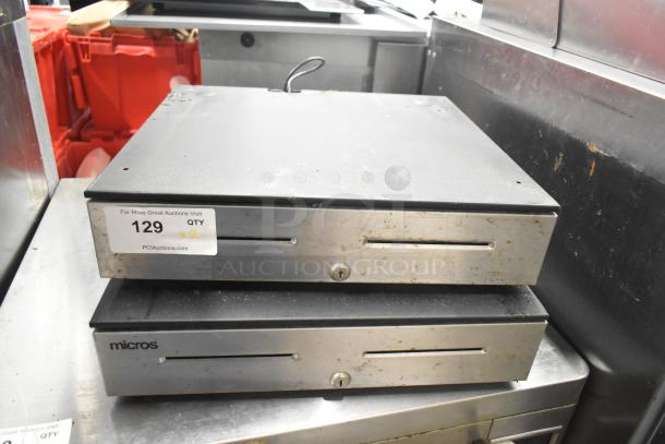Two metal cash drawers, Micros brand, showing wear. Stackable design with keyholes. Auction label reads "129 x2".