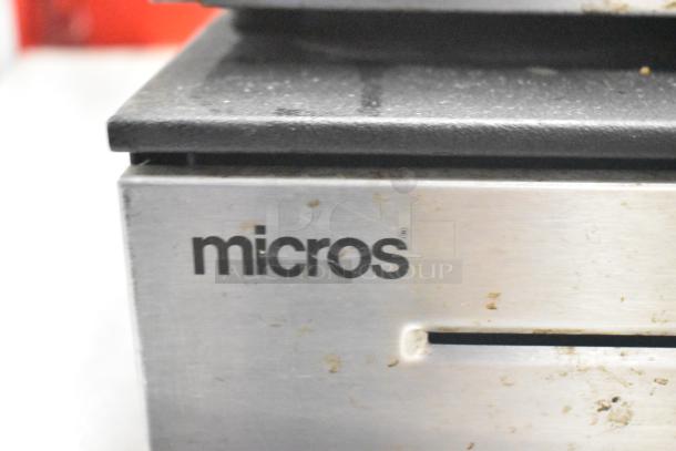2 metal cash drawers, brand "Micros." Used condition with visible surface marks. Secure cash slot shown.