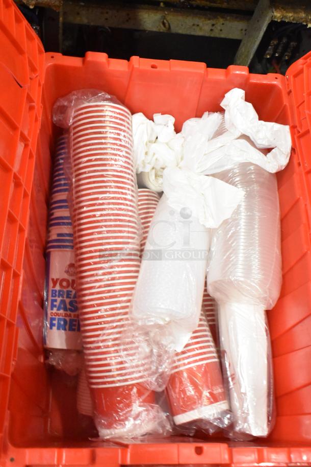 Red poly bin filled with contents including wrapped red cups, white napkins, and clear utensils. Auction for 13 bins total.