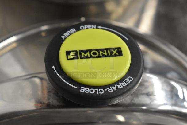 Monix Classica Pressure Steamer Pot lid, featuring a lime green Monix-branded knob with open/close directions in English and Spanish.