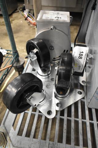 Lot of 4 brand new scratch and dent casters, black rubber wheels, mounted on metal plates. Visible tags indicate auction details.