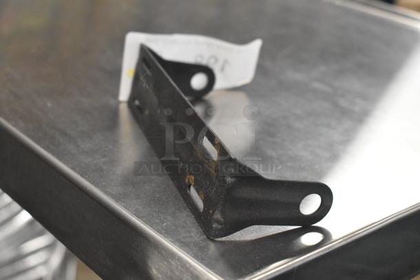 Black metal hanging holder with two slots and one round hole, resting on a metal surface. Worn condition visible.