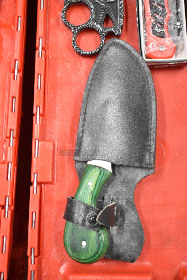 Assorted items in red case: black brass knuckles, green-handled knife in black sheath, unopened red pocket knife.