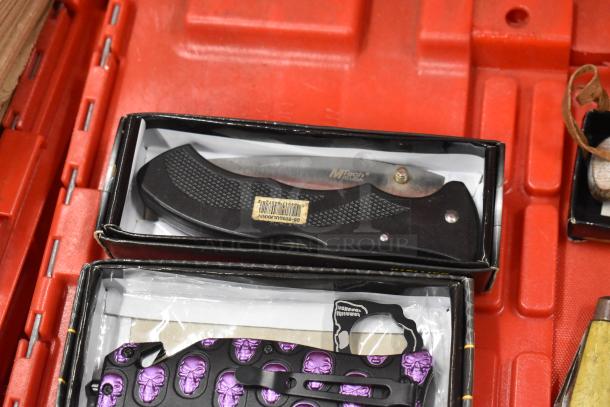 MTech USA folding knife with black handle in box, featuring textured grip and gold pivot. Skulls design visible on nearby item.