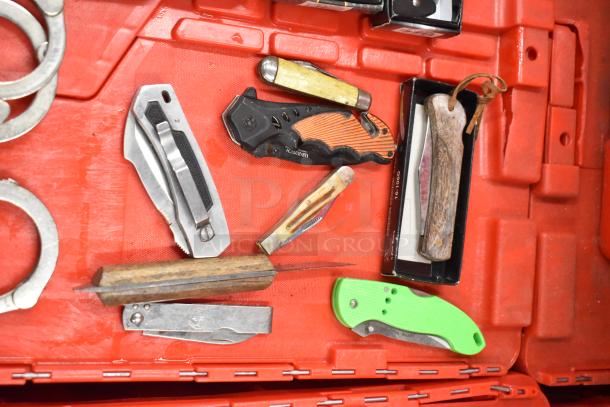 Assortment of handcuffs, brass knuckles, and various pocket knives on a red background. Mixed materials and styles.