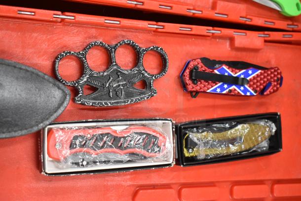 Assorted items including decorative brass knuckles, pocket knives with patterned handles, and packaged knives on a red background.