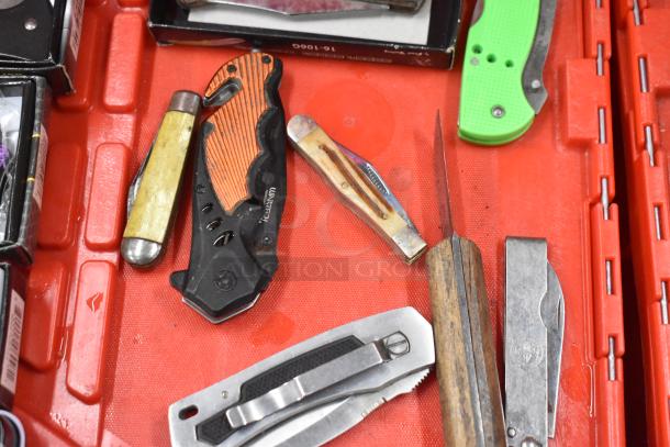 Assorted lot of pocket knives with various designs and conditions on a red tray; includes brands like VANTEX.