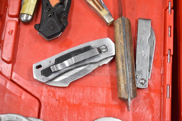 Assorted items, including various pocket knives, displayed on a red surface; condition varies among pieces.