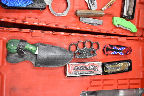 Assorted items including handcuffs, brass knuckles, and pocket knives displayed on a red surface. Various colors and designs.