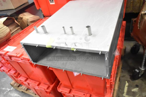 Stainless steel metal box, rectangular shape with protruding pipes and bolts, minor surface scratches, sturdy construction.