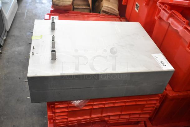 Stainless steel metal box with protruding pipes, slightly scratched surface, numbered tag "205", placed on red crates.