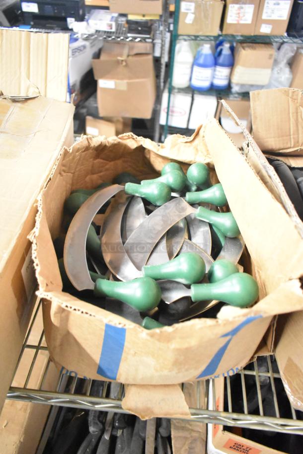 Open box of assorted stainless steel knives with green handles, featuring filet, serrated, and rocking cutter types.