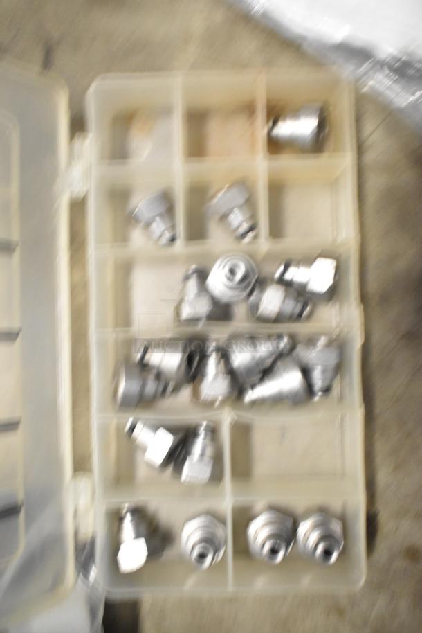 Blurred image of metal fittings in a plastic organizer box. Condition and specific details unclear.