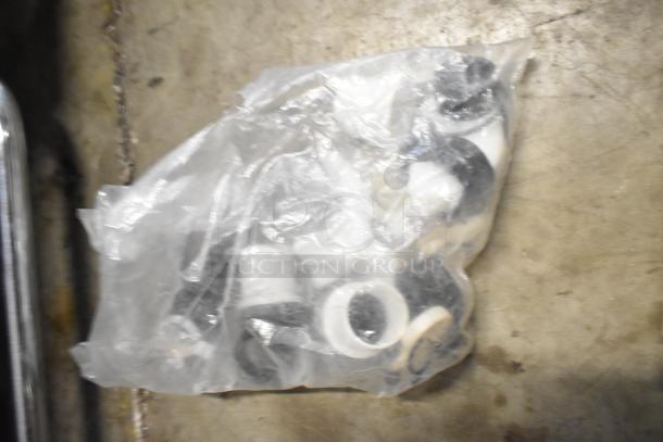 Bag of assorted white and black plastic rings on a concrete floor, part of a tier lot with brew baskets and drip trays.