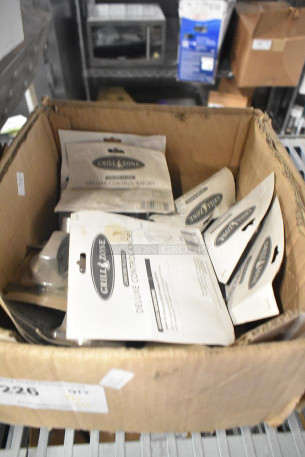 Cardboard box containing various items including Grill Zone deluxe control knobs packaging, part of a tier lot auction.
