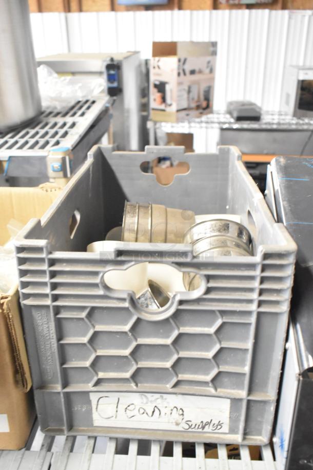 Gray storage crate containing various items including mixing cup collar and fluorescent sockets, labeled "Cleaning Supplies."