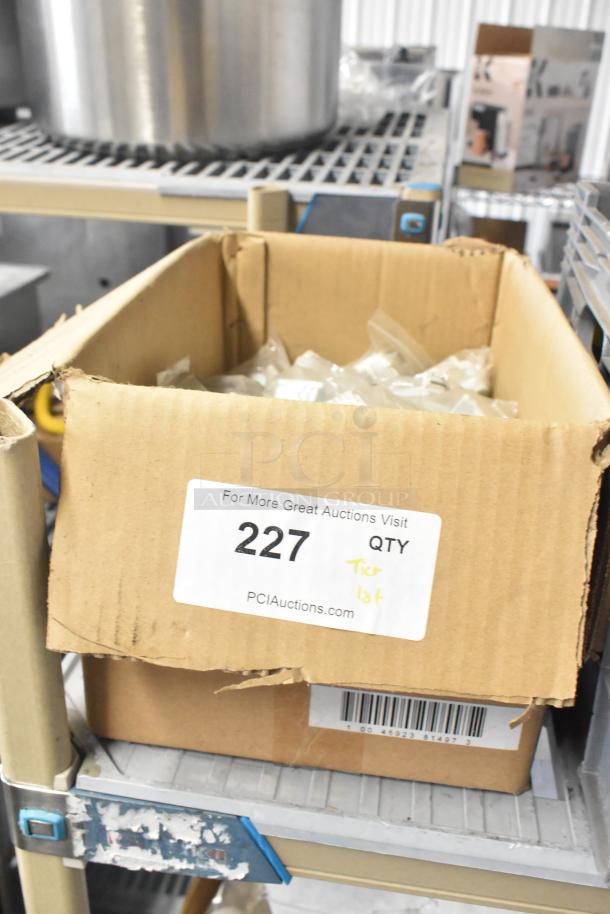Cardboard box labeled "227" containing various items, including mixing cup collar and fluorescent sockets, on metal shelf.