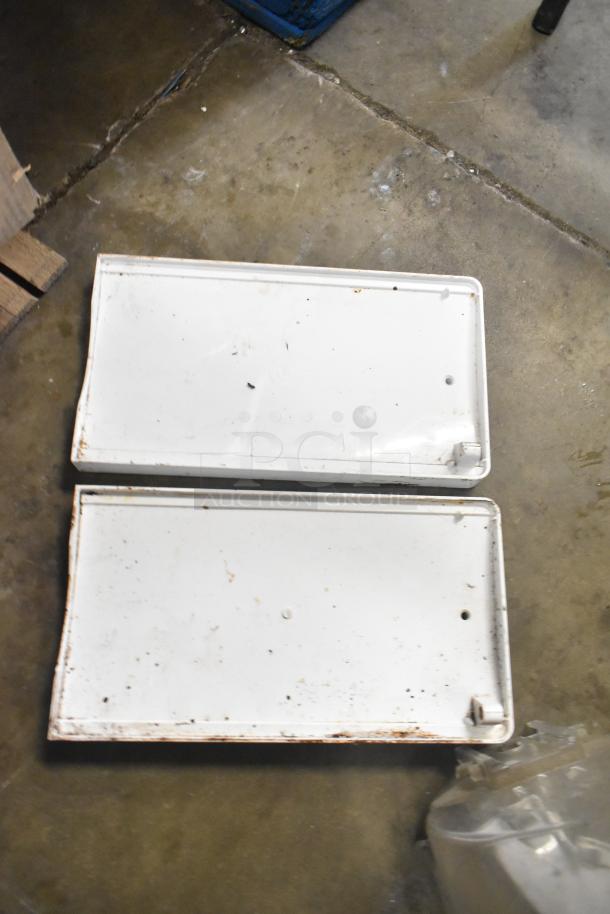 Two worn white metal kickplates, slightly rusted, from Turbochef, on a concrete floor.