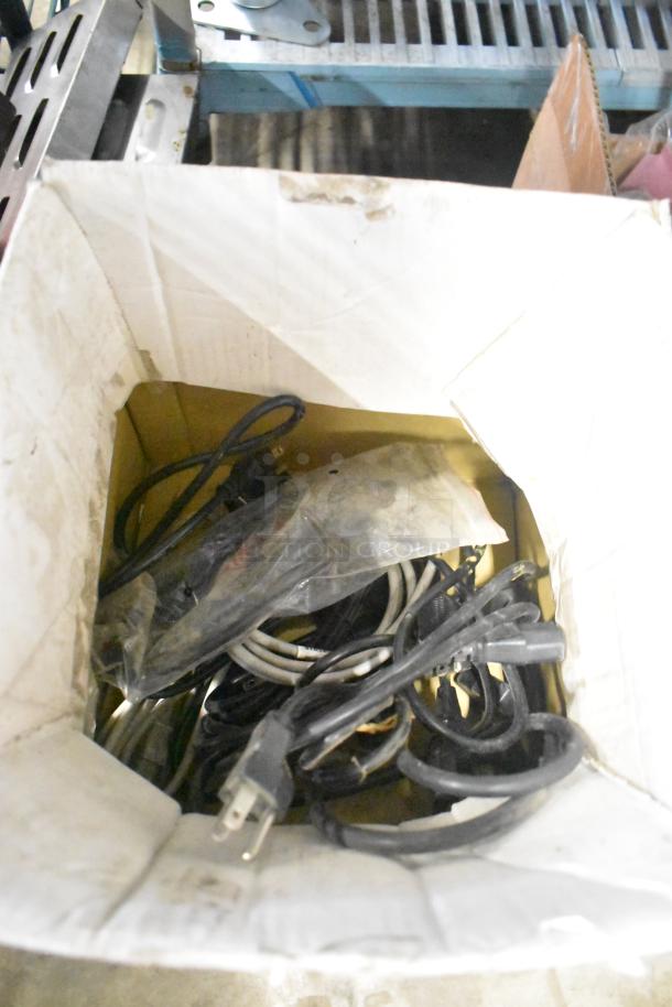 Box of mixed power cables and miscellaneous hardware accessories in used condition. Stored inside a cardboard box.