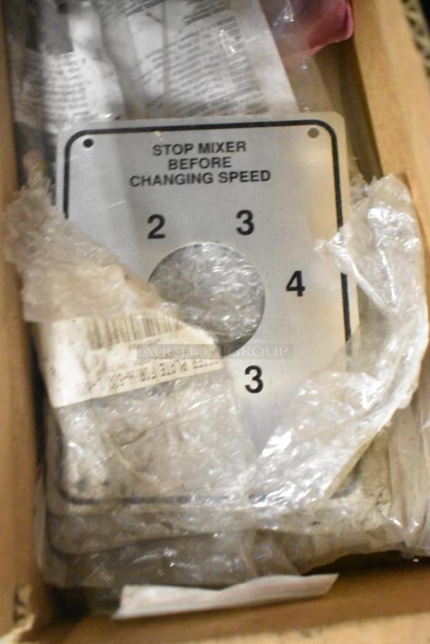 Box with various items including a "STOP MIXER BEFORE CHANGING SPEED" metal plate, wrapped in plastic.