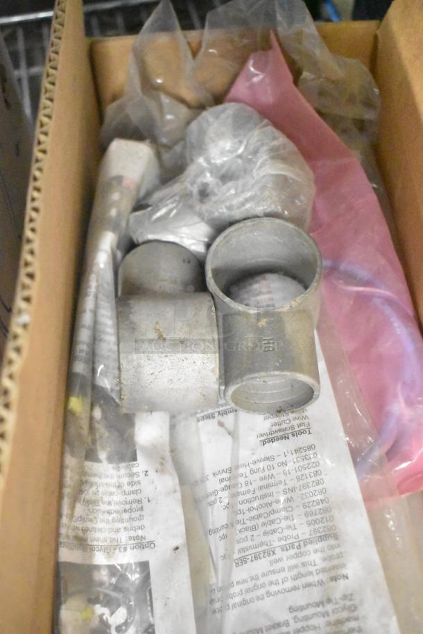 Box of miscellaneous items including metal connectors, pink plastic sheet, and packaging. Items appear used.