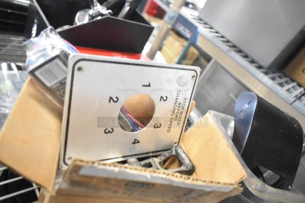 Tiered lot of various items, including ice cream machine lids, ice head panel with switch kit, and portafilters. Includes Danfoss filter drier, Bunn dispenser spouts, and mixer control panel. Items in mixed condition in cardboard box.