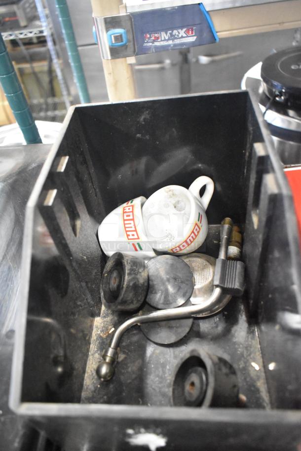 Assorted small kitchen and machine parts, including ROMA espresso cups, portafilters, and rubber components in a black bin.