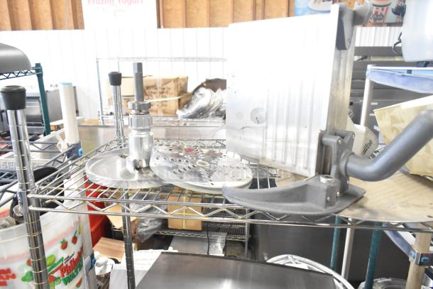 Tier lot including Pelican head blade, grating/slicing blades for food processor, meat slicer carriage on metal rack.