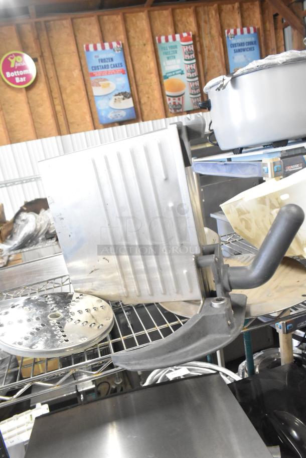 Tiered lot featuring a Pelican head blade, food processor grating/slicing discs, and a meat slicer carriage on a wire rack.