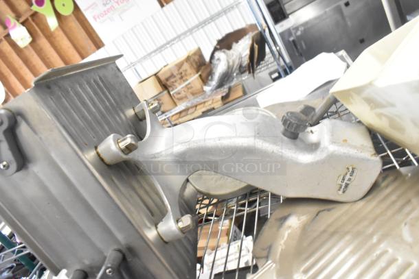 Auction lot with Pelican head blade, food processor grating/slicing blades, and meat slicer carriage, shown on metal rack.