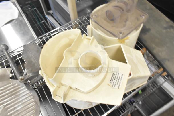 Lot of kitchen items including Pelican head blade, food processor blades, and meat slicer carriage, shown on wire rack.