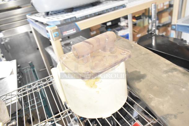 A miscellaneous lot including a Pelican head blade, food processor blades, and a meat slicer carriage, all on a wire shelf.
