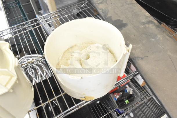 Lot of kitchen equipment items including a Pelican head blade, food processor parts, and a meat slicer carriage. Items on wire shelf.