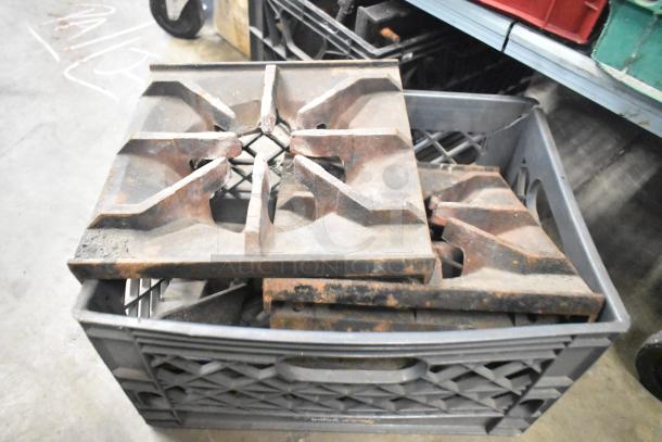 Nine metal range grates, stacked in a crate, showing signs of wear and rust, ideal for industrial use.