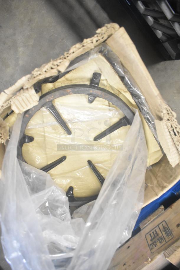 Nine metal range grates in cardboard box, partially wrapped in plastic, showing slight rust. Suitable for stove replacement.