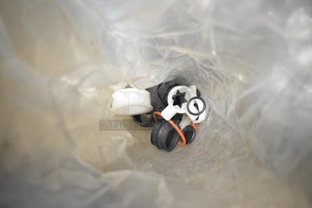 Various machine parts including ice cream and beverage adapters in a transparent bag. Some parts are white and black plastic.