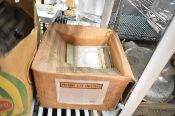 Cardboard box containing various ice cream machine parts, labeled "Packing List Enclosed," on a metal shelf. Items appear used.