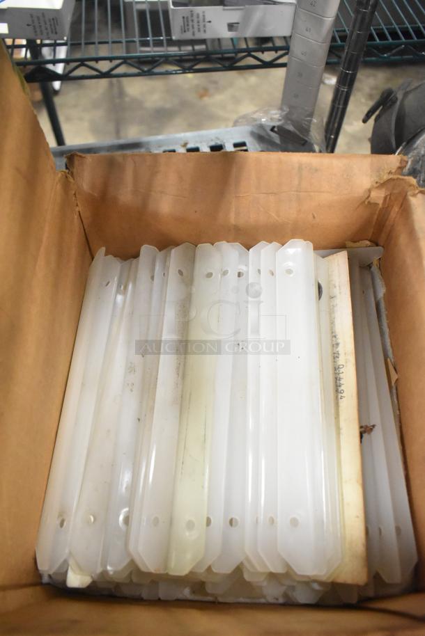 Box containing Taylor ice cream machine parts, featuring white plastic components with holes, in good condition.
