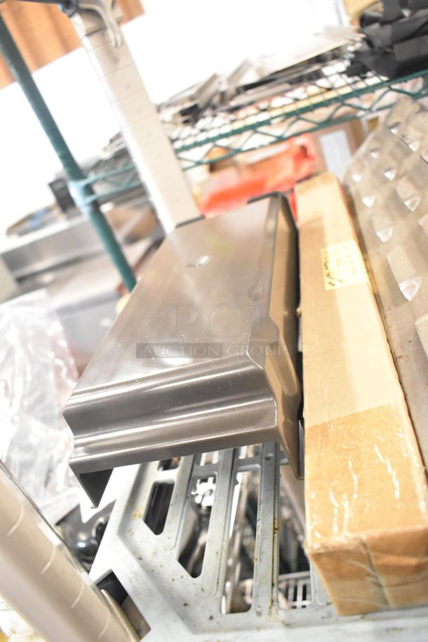 Assorted industrial parts including a stainless steel kickplate and drip trays on shelf, showing new condition.