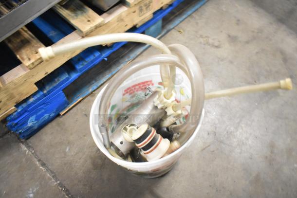 Bucket with miscellaneous kitchen equipment, including hoses and metal parts, placed on a wooden pallet.