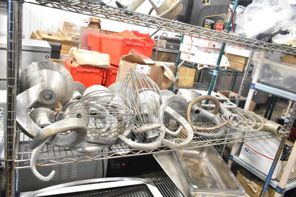 15 Hobart mixer attachments on a metal shelf, including dough hooks, paddle whips, and whisk. Various conditions.