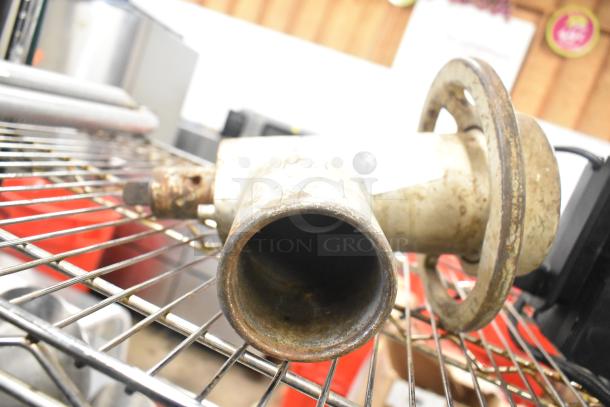 Metal meat grinder attachment, used condition, visible wear and rust, placed on a wire rack, no branding visible.