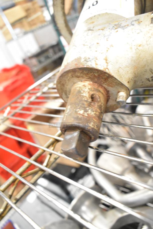 Rusty meat grinder attachment on a metal rack, showing attachment point and wear. Ideal for parts or restoration.