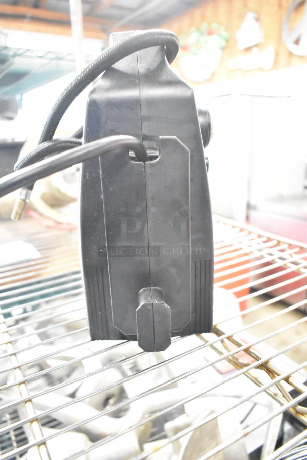 Duracell jump starter and compressor, black, with attached cables. Appears in used condition on a metal shelf.